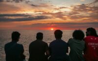 Friends watch the sunset over the ocean.